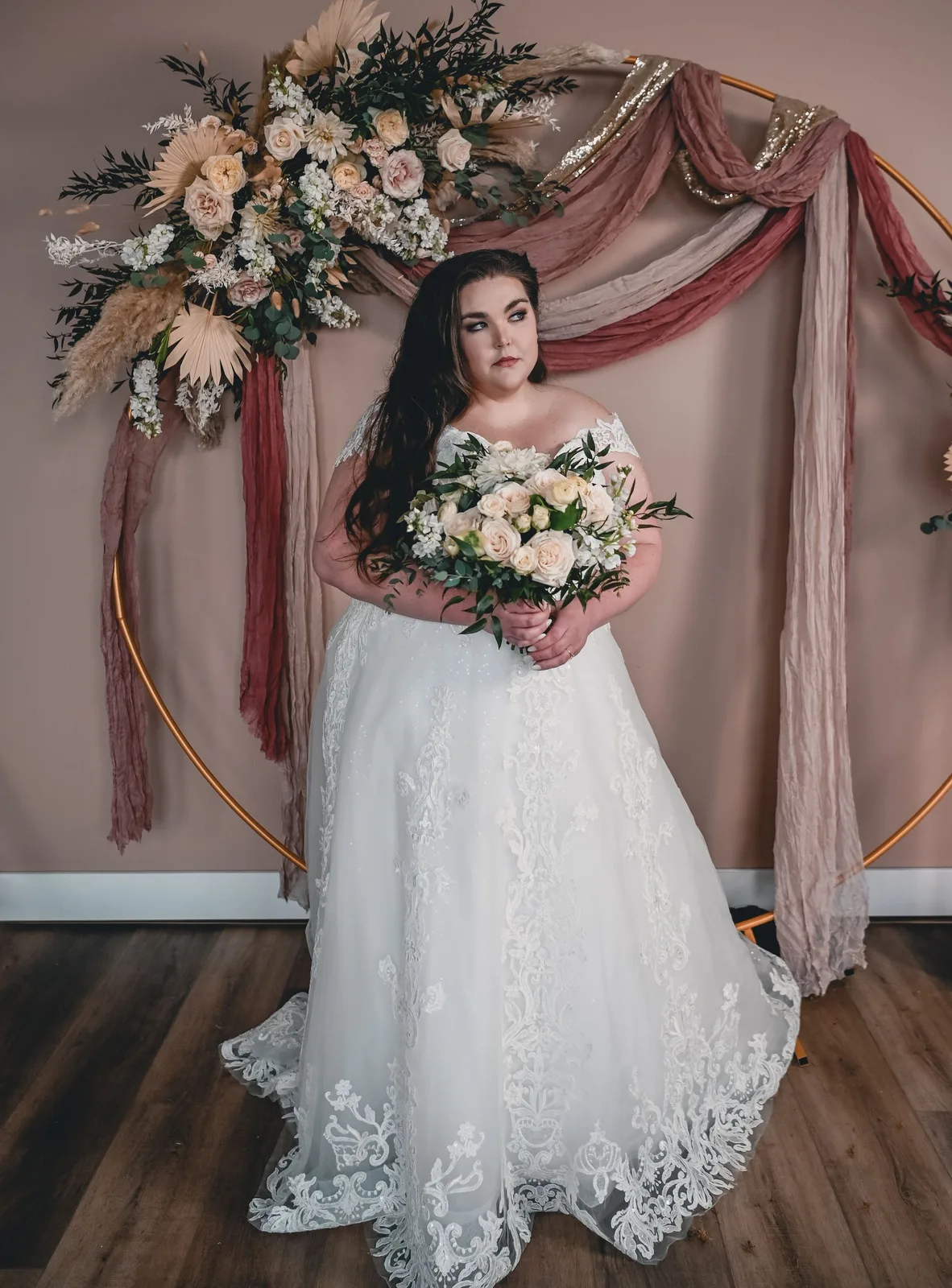 Bride in a fitted gown with a bouquet, blush backdrop