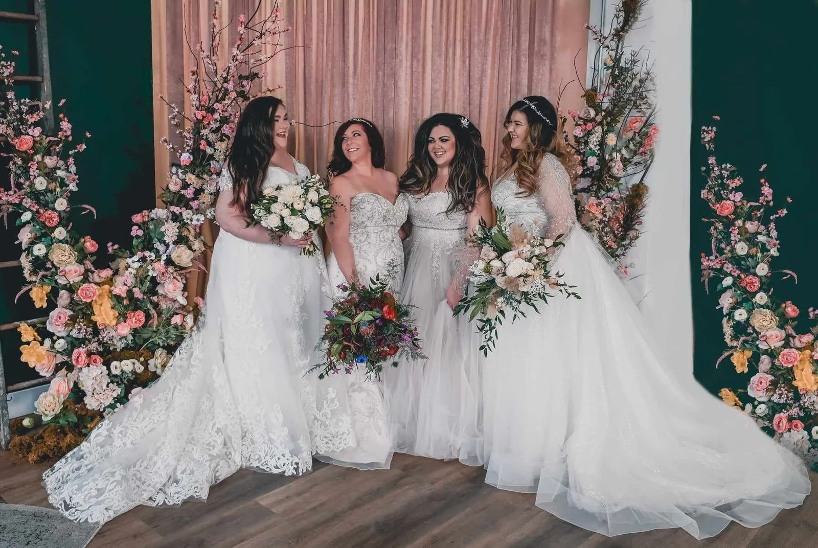 Bride in a lace gown holding a bouquet against a blush backdrop