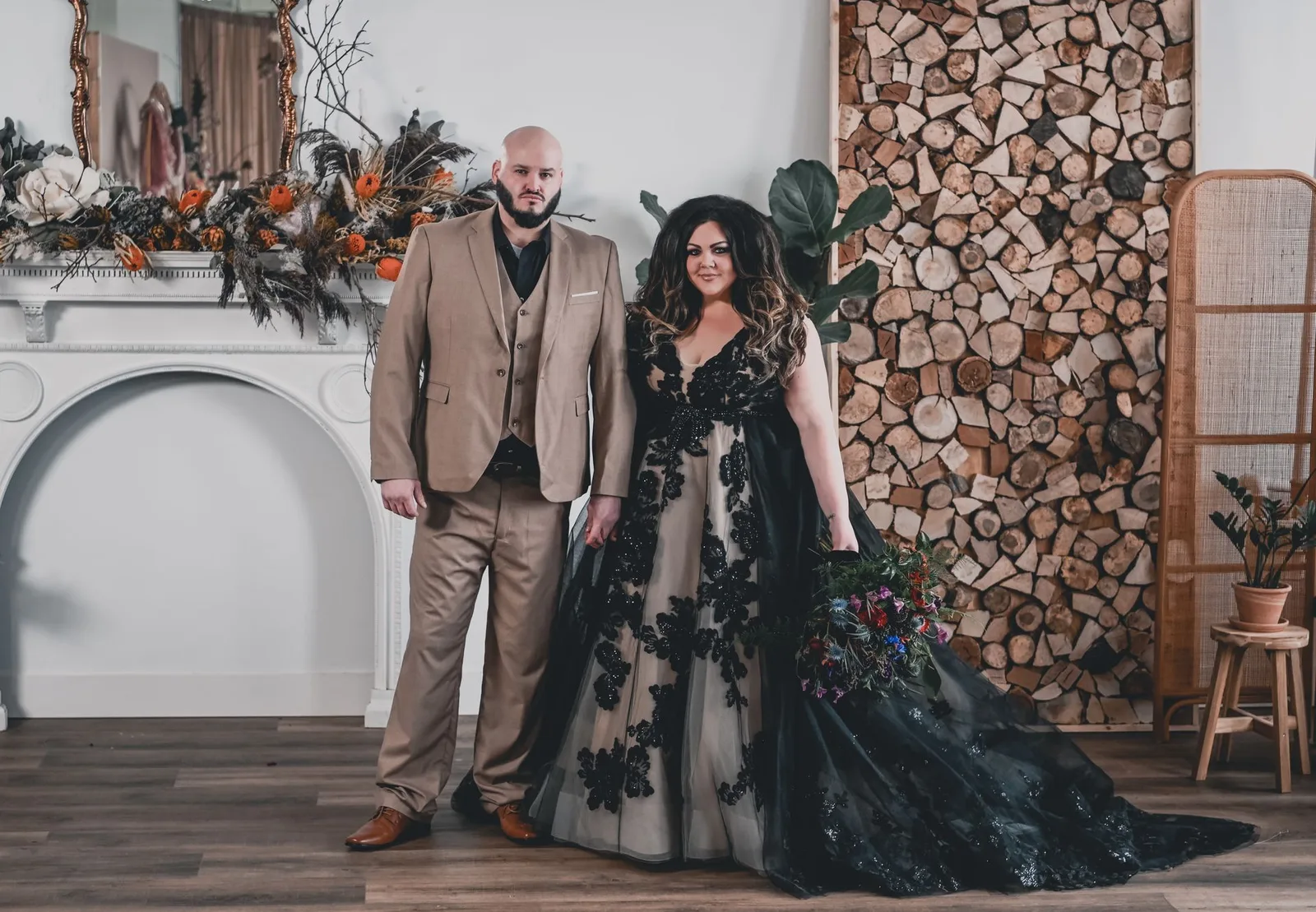 Couple, bride in a black gown by a floral wall